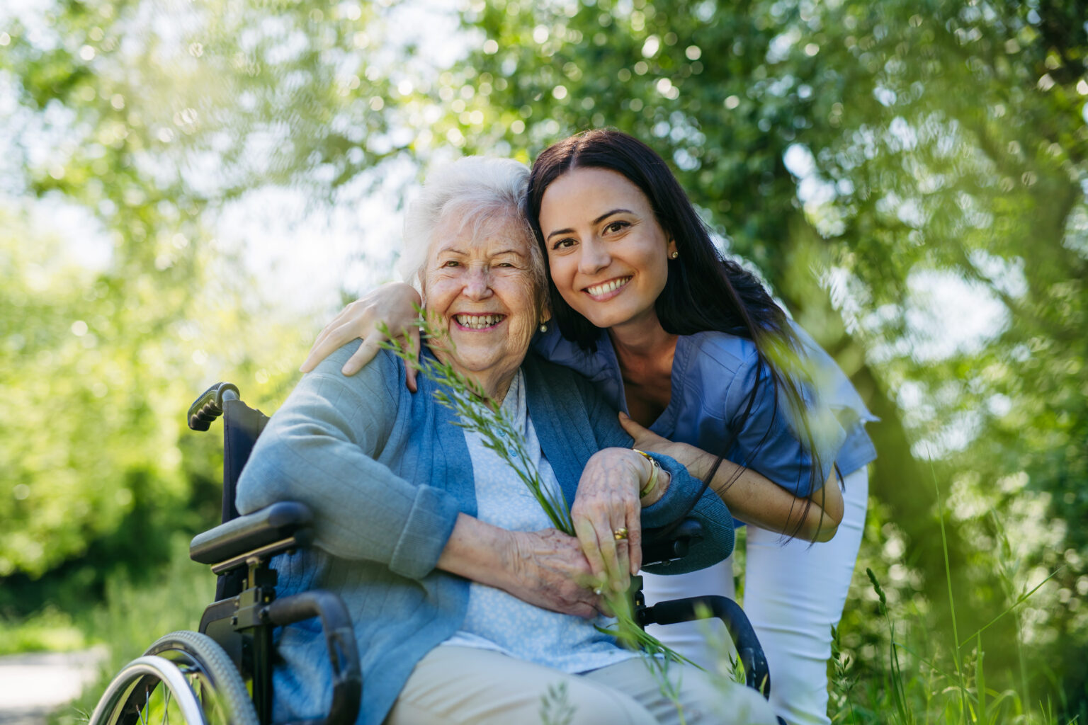 Pflegekraft und Seniorin im Rollstuhl genießen einen Spaziergang im Grünen