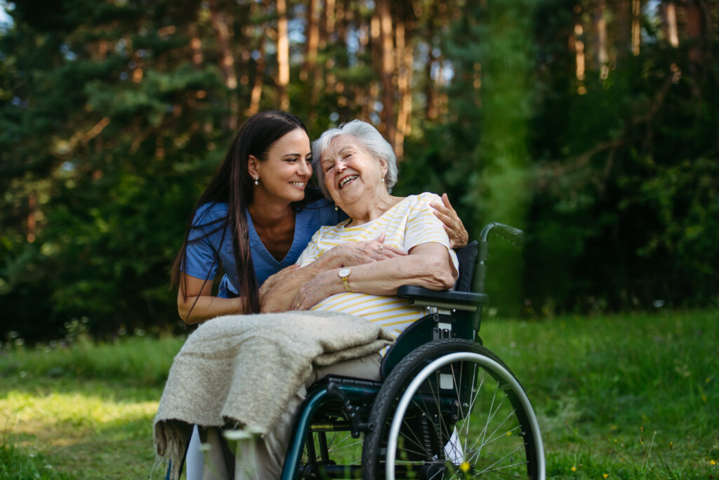 Pflegekraft begleitet eine ältere Dame im Rollstuhl bei einem Spaziergang